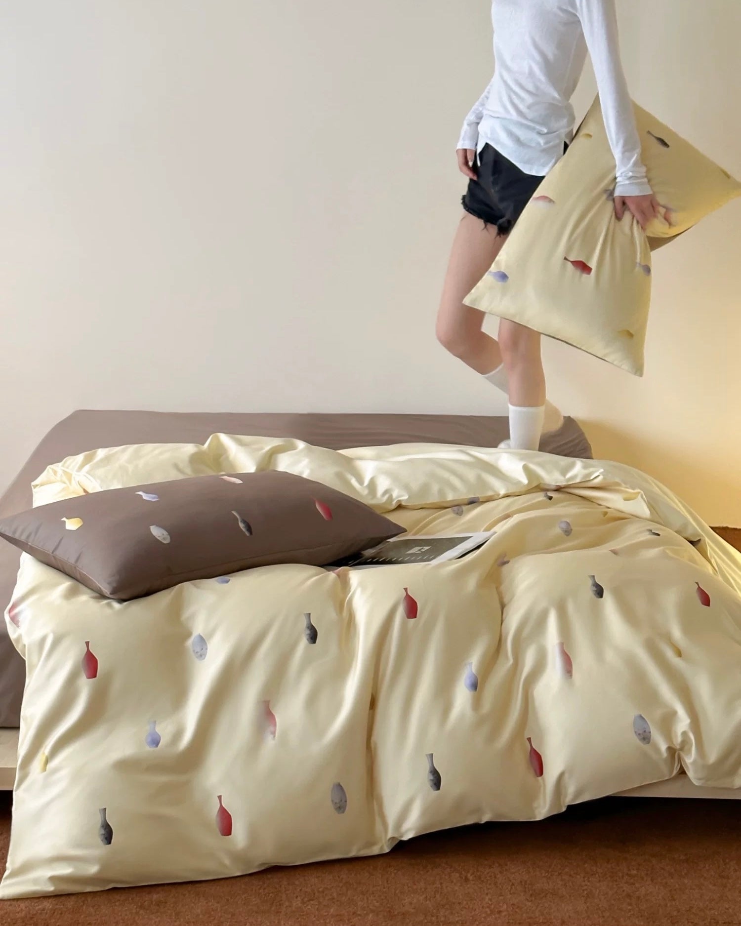 Bed with beige bedding featuring small colorful bottles, a person standing in the background.