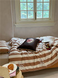 Bed with striped bedding and a pillow, next to a window with a view of greenery.