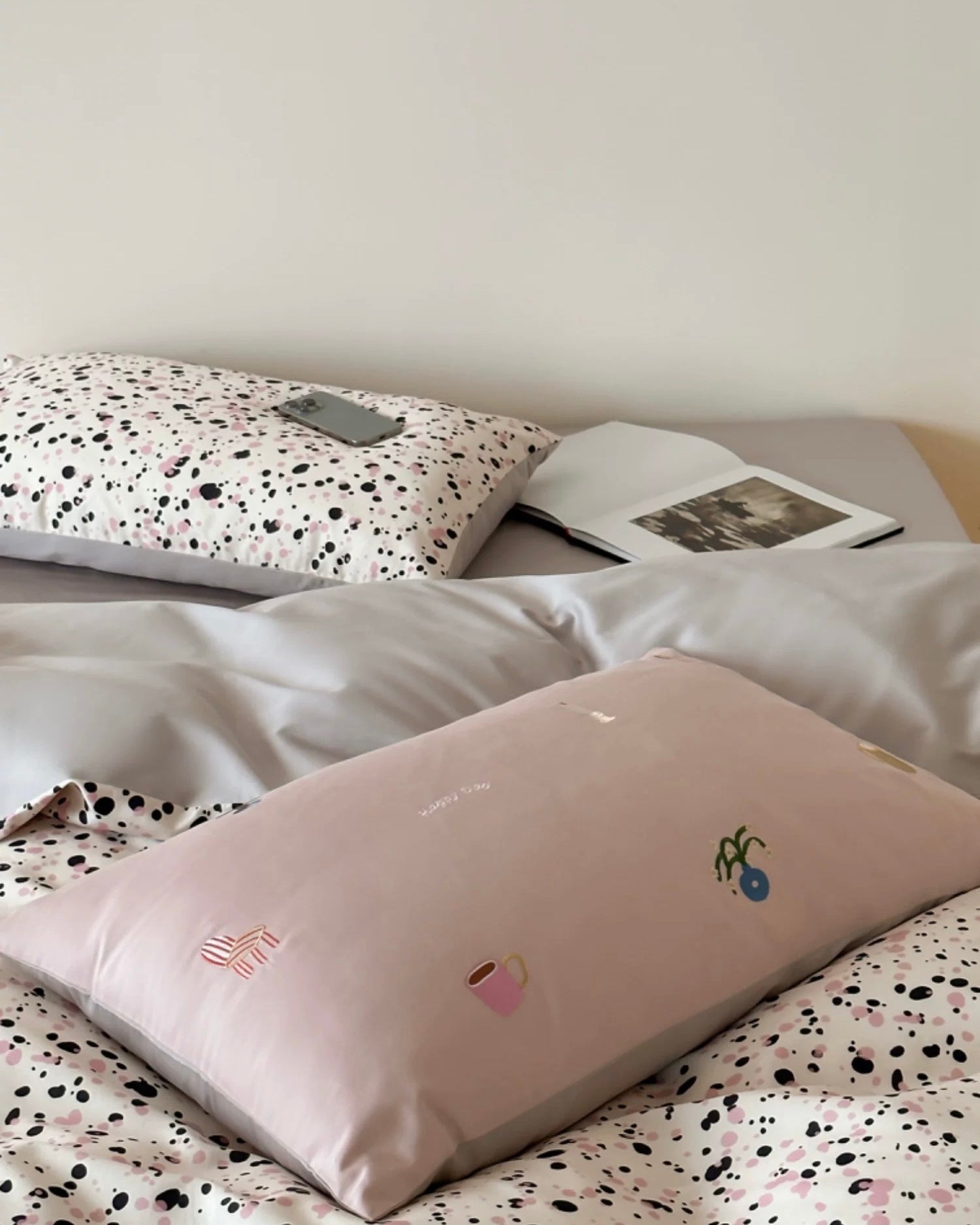 Neatly made bed with a pillow featuring cartoon designs on a polka dot blanket.