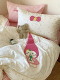 Children's bedroom with pink checkered pillow, embroidered character on bedding, and teddy bear.