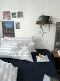 Bedroom with striped pillows, a plant, and a small table with a cup and cookies.