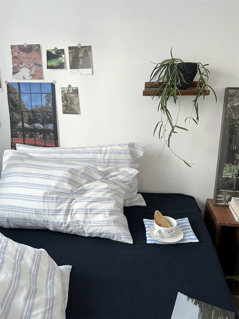 Bedroom with striped pillows, a plant, and a small table with a cup and cookies.