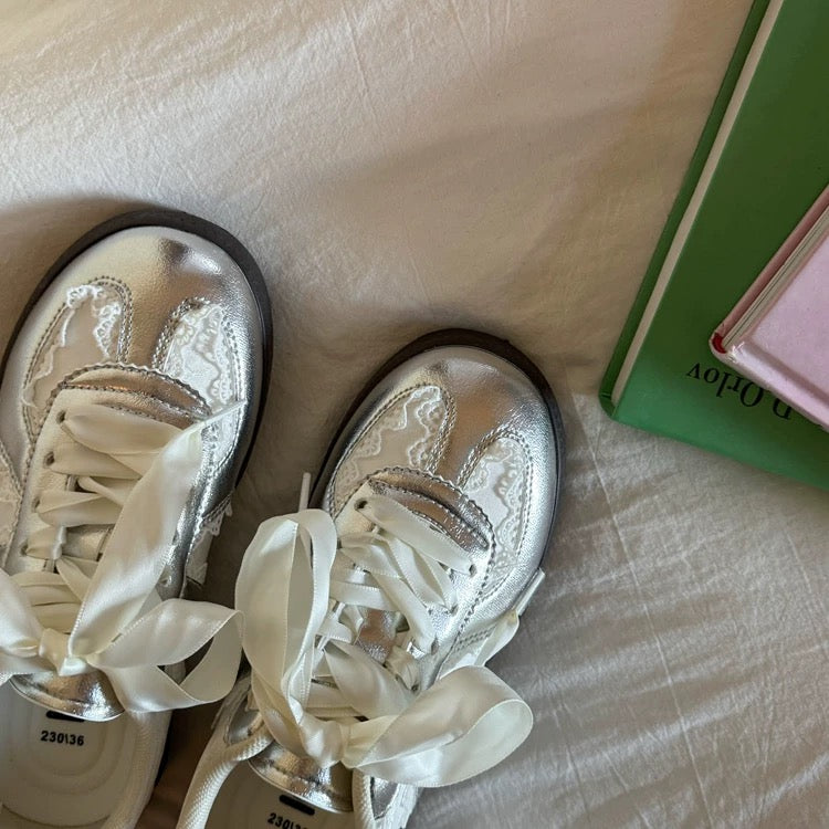 Silver high-top sneakers with white laces on a light fabric surface.