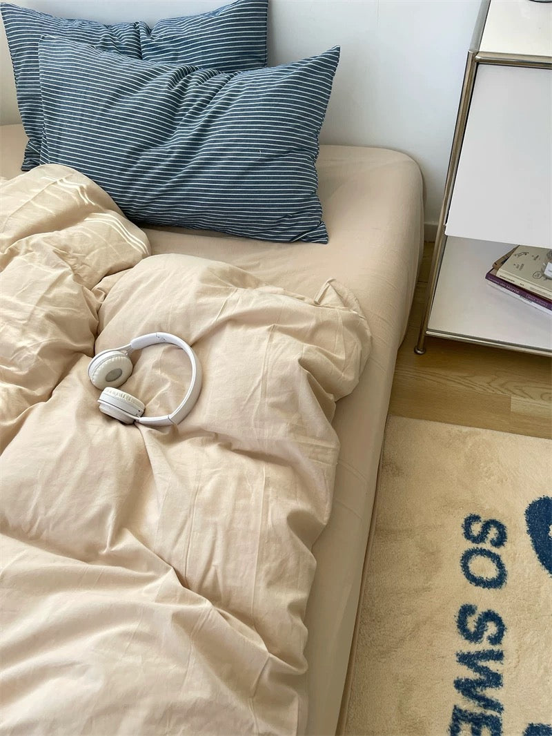 Beige bed with blue striped pillows and a white comforter, next to a nightstand.