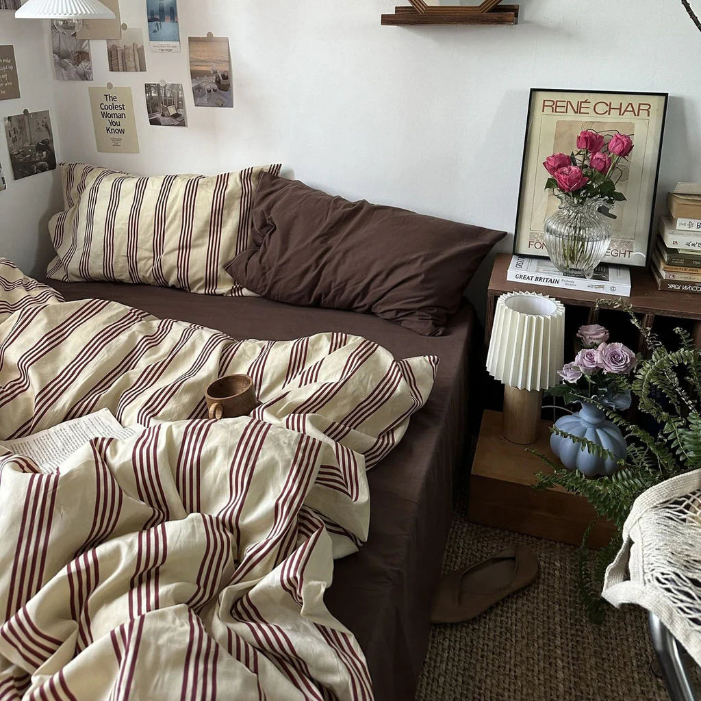 Bedroom with striped bedding and a vase of flowers on a nightstand.