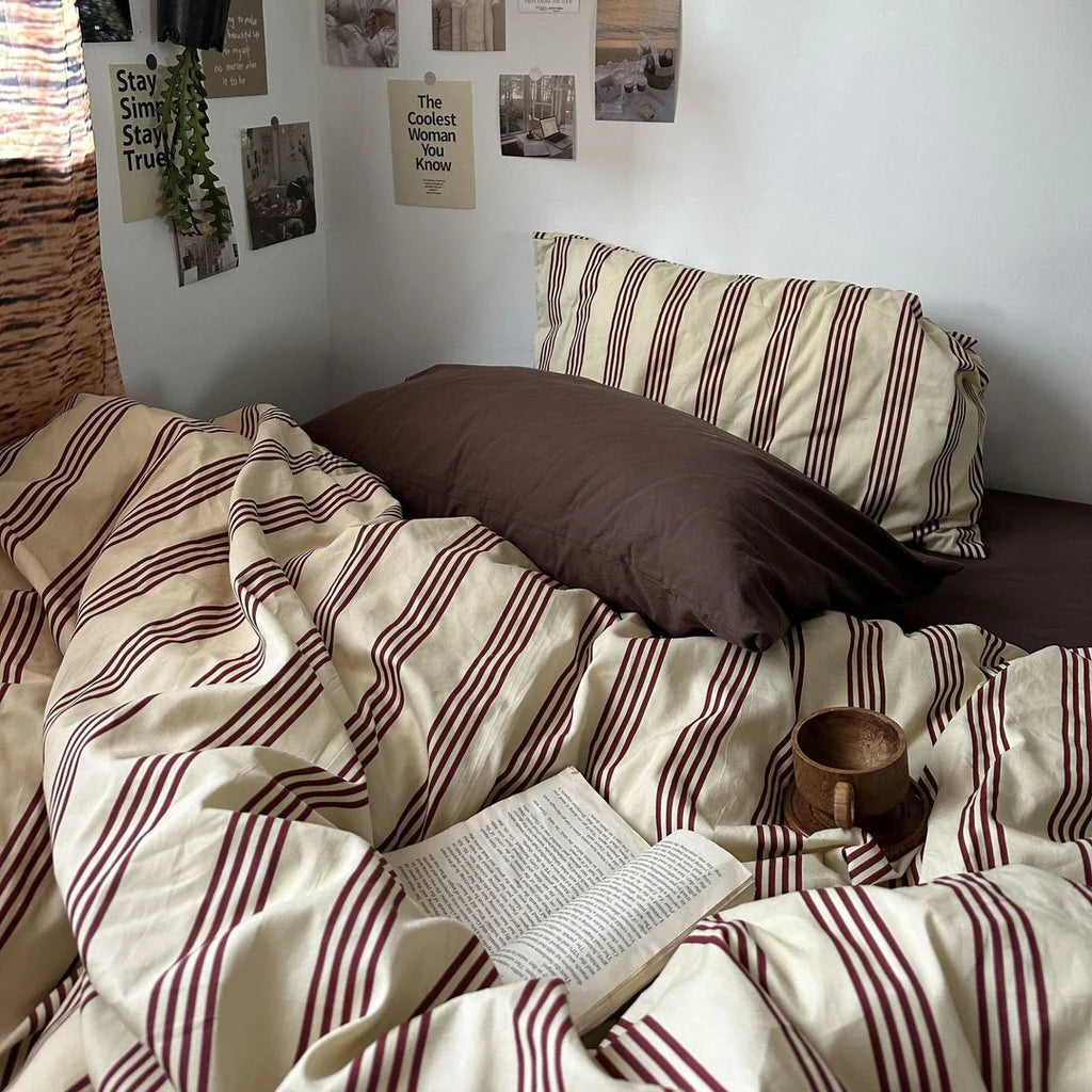 Bedroom with striped bedding and a vase of flowers on a nightstand.