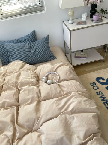 Beige comforter on a bed with blue pillows, nightstand, and decorative items.