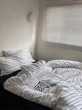 Unmade bed with striped bedding in a room with a window and wall decor.