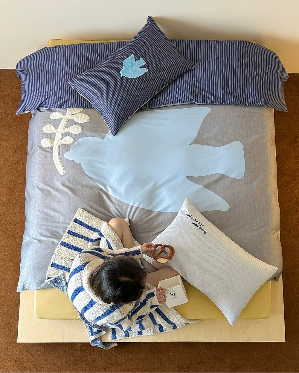 Bed with gray bedding and pillows against a beige wall