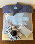 Person lying on a bed with blue and gray bedding, holding a phone.