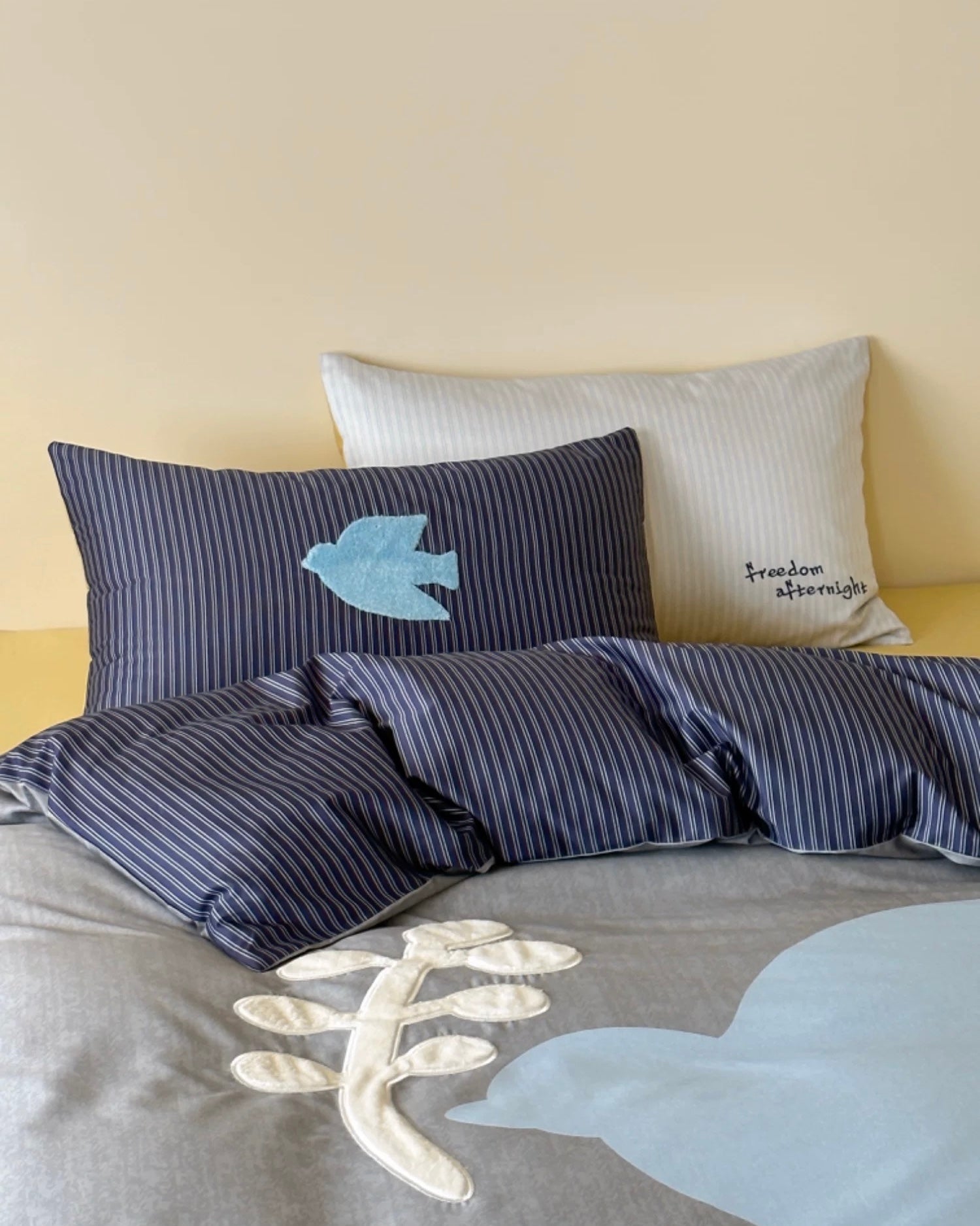 Striped bedding set with fish designs on a bed against a beige wall.