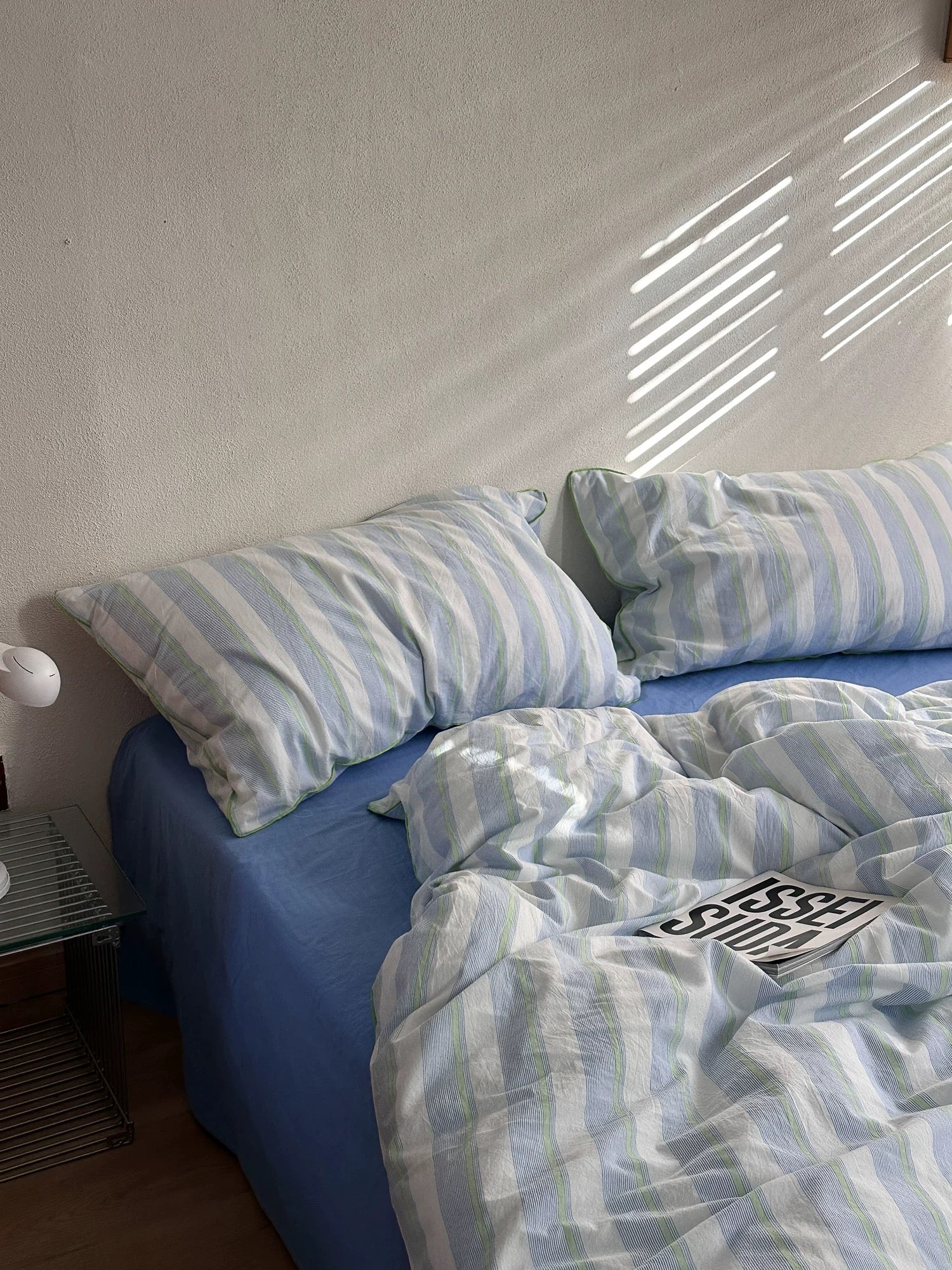 Blue bed with striped bedding and pillows against a white wall.