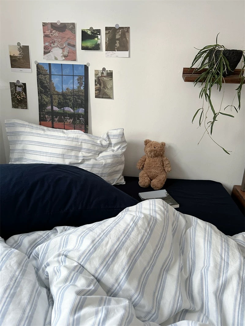 Bedroom with striped bedding, pillows, a teddy bear, and wall decorations.