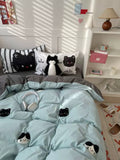 Bed with light blue comforter featuring black cat designs, surrounded by a cozy room setting.