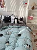 Light blue comforter with cat designs on a bed in a room with a shelf and lamp.
