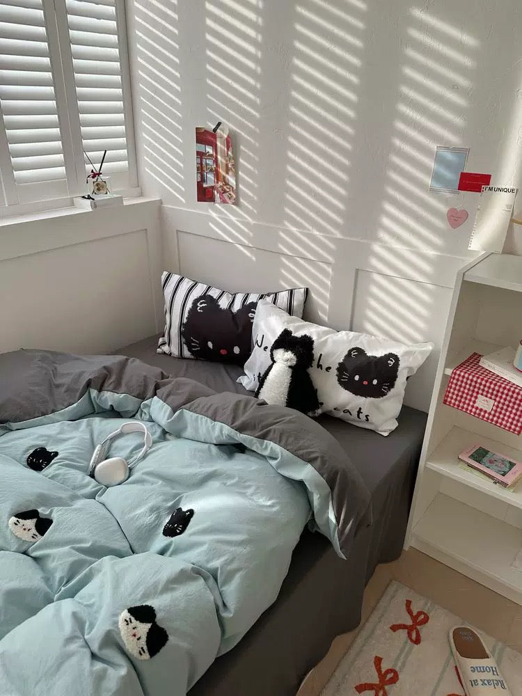 Bedroom with cat-themed bedding and pillows, sunlight filtering through shutters.