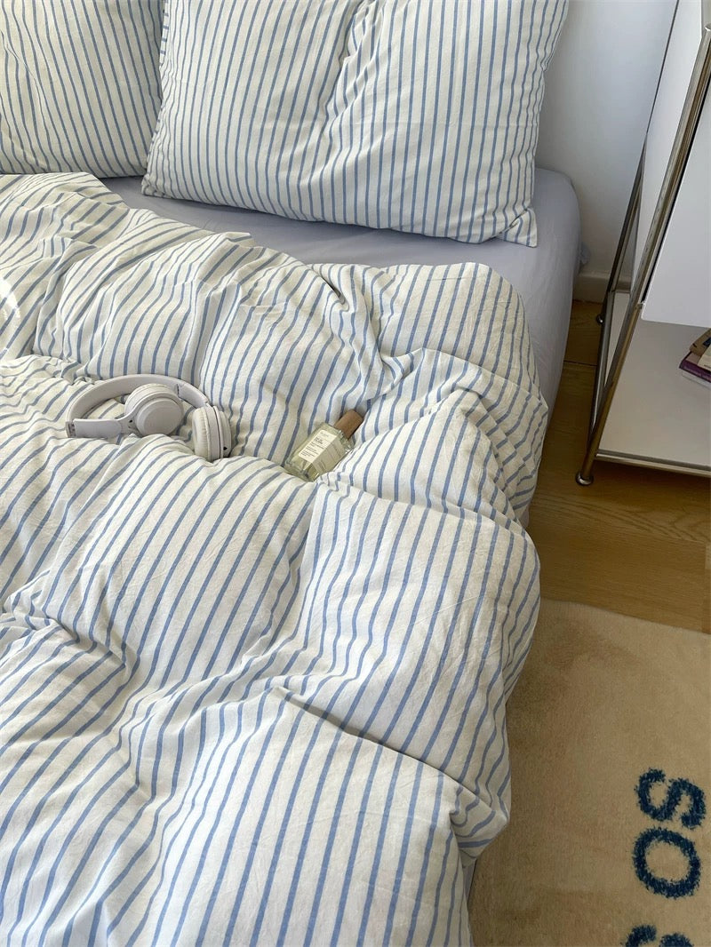 Striped bedding on a bed with a white pillow and a small object on the floor.