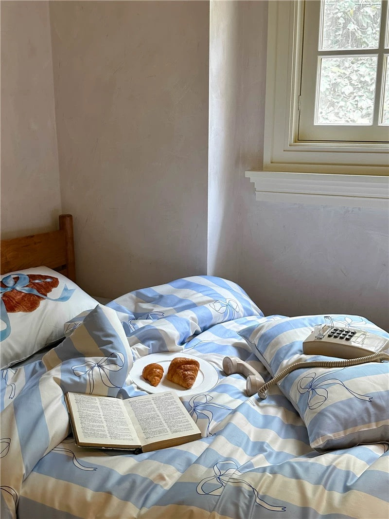 Bed with blue and white striped bedding, a plate of pastries, and a telephone on a nightstand.