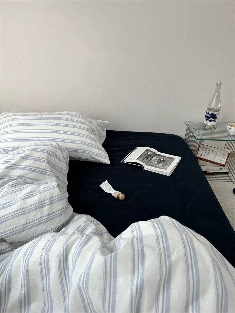 Bed with striped bedding and pillows, nightstand with books and a bottle.