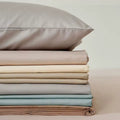 Stack of folded bed sheets and pillowcases in neutral colors on a light background