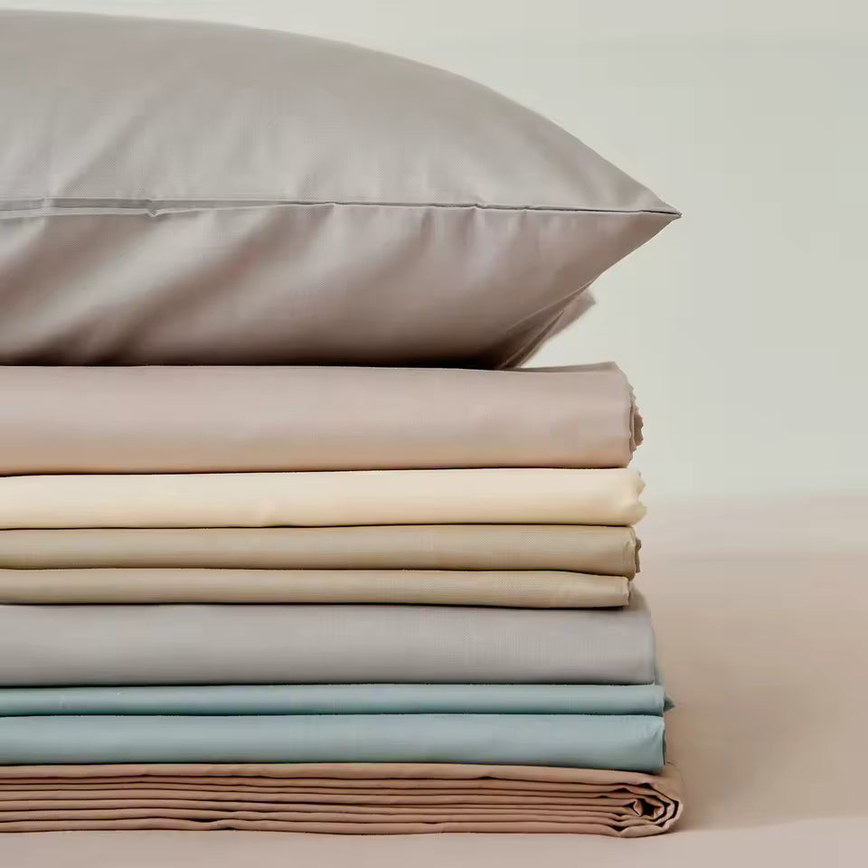 Stack of folded bed sheets and pillowcases in neutral colors on a light background