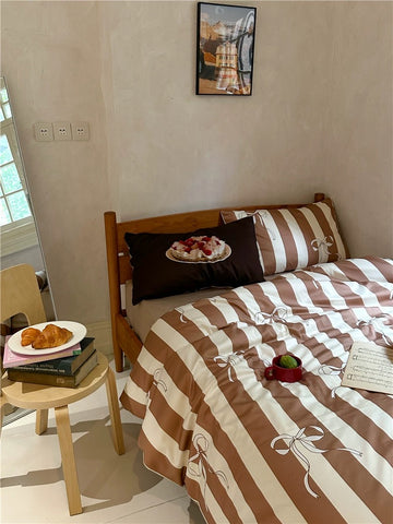 Bedroom with a bed covered in brown and beige striped bedding, pillows, and small table with food.