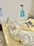 Neatly made bed with light-colored bedding in a room with a lamp and wall decor.