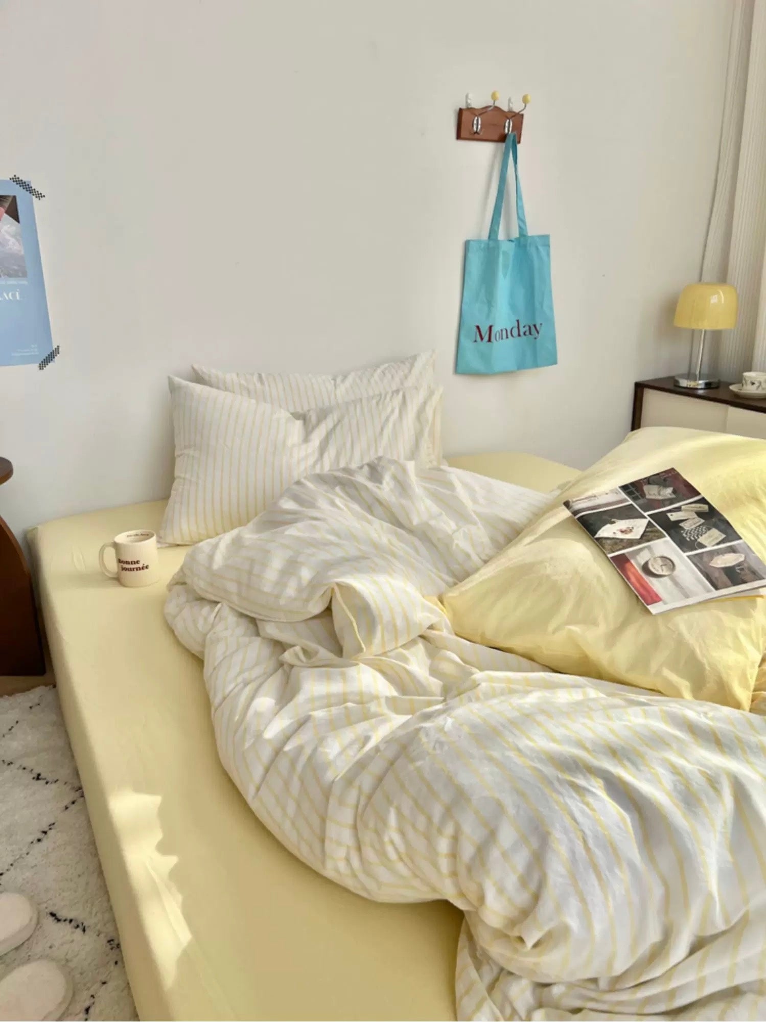 Neatly made bed with light-colored bedding in a room with a lamp and wall decor.