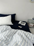 Bed with striped bedding and pillows, nightstand with books and a clock.
