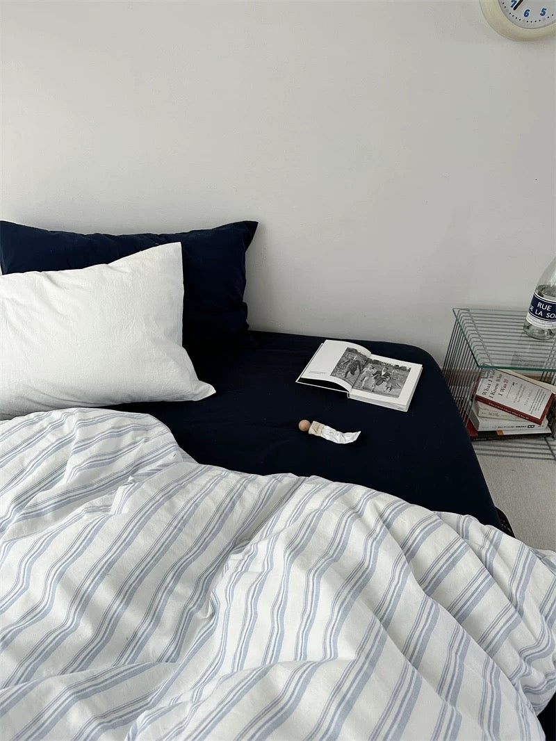 Bed with striped bedding and pillows, nightstand with books and a clock.