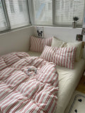Bed with red and white striped bedding and pillows in a room with window blinds.