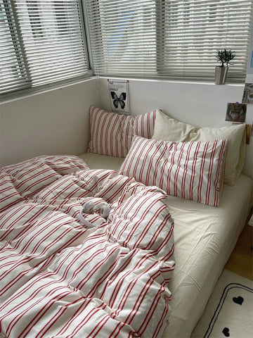 Bed with red and white striped bedding and pillows in a room with window blinds.