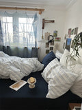 Cozy bedroom with striped bedding, pillows, and a window with blue curtains.