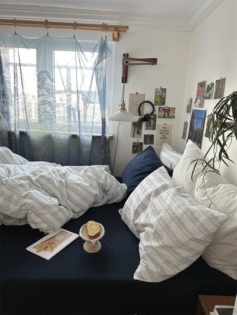 Cozy bedroom with striped bedding, pillows, and a window with blue curtains.