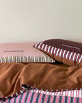 Bedding set with striped and solid color pillows on a bed.