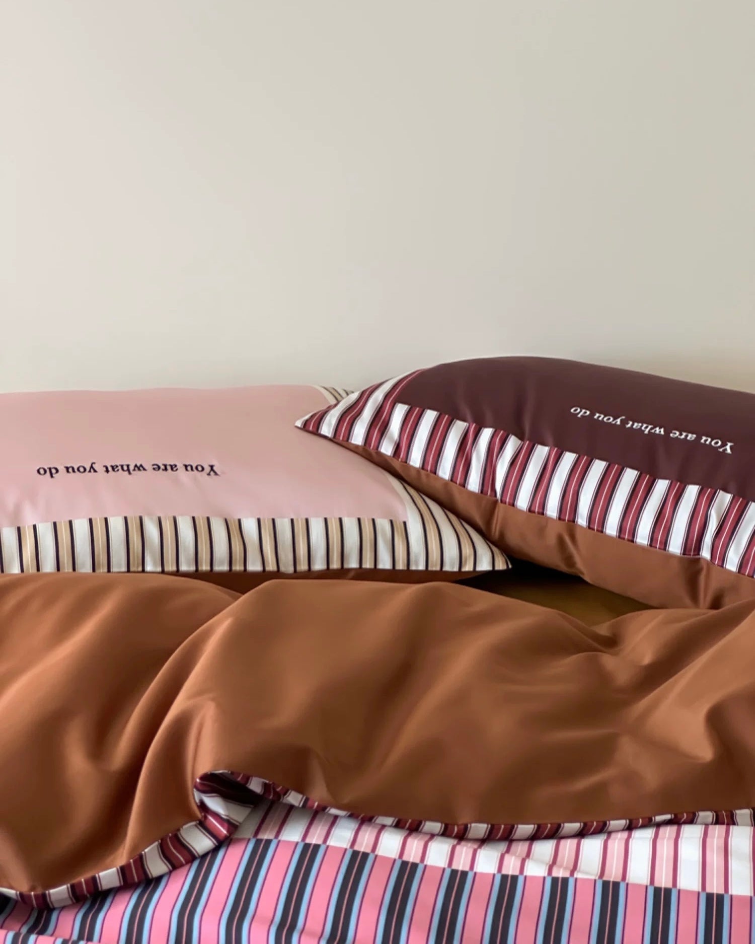 Bedding set with striped and solid color pillows on a bed.