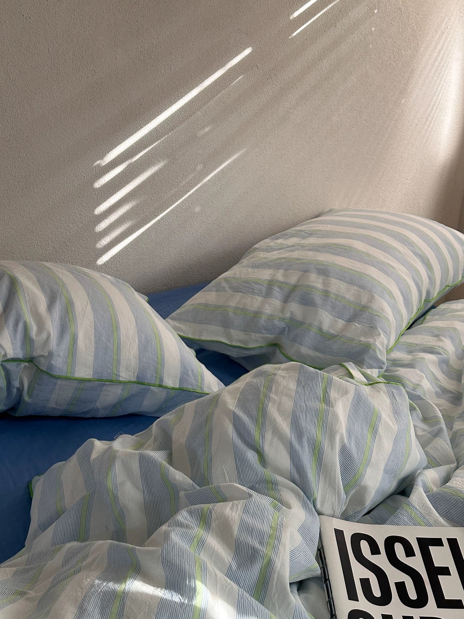 Striped bedding with pillows on a bed, featuring the brand 'Issey Miyake'.