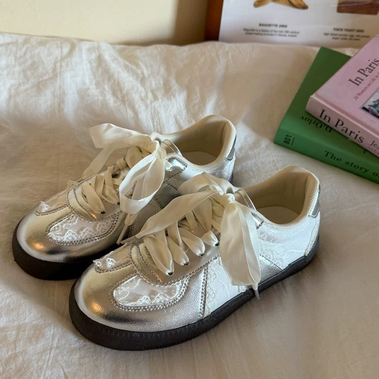 Pair of white sneakers with black soles on a light-colored surface.