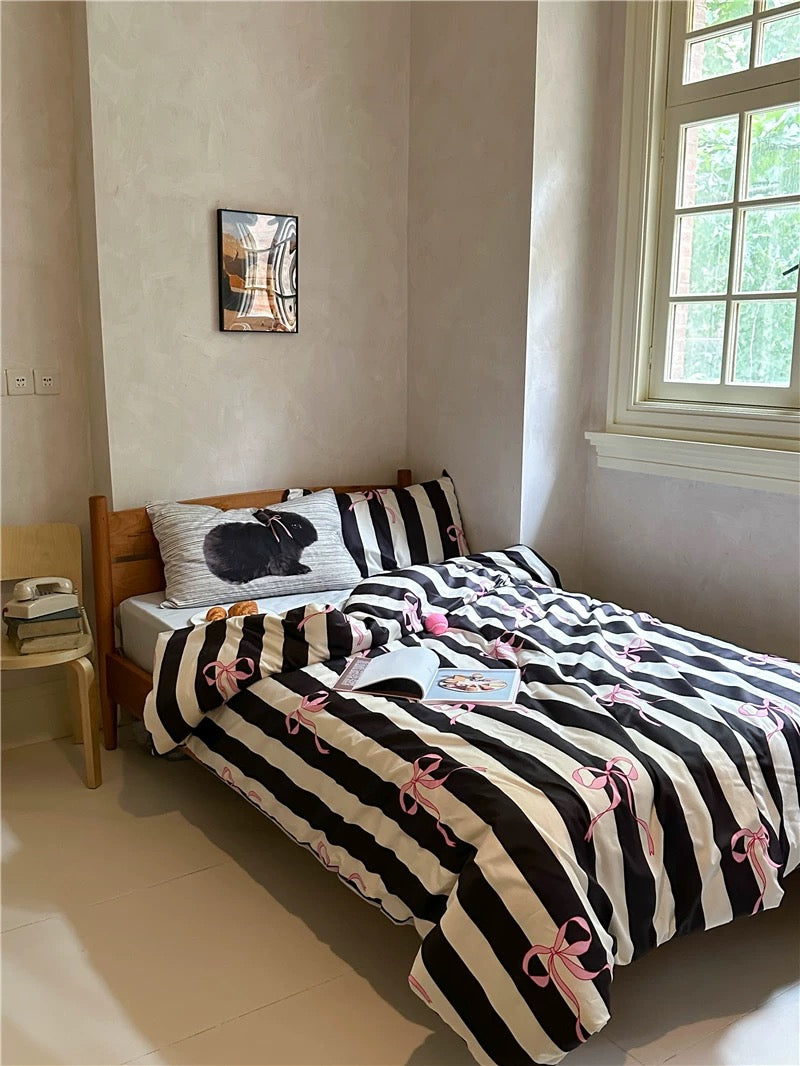 Bed with striped bedding and decorative pillows in a room with a chair and table.