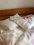 Bed with pink and white striped bedding and a wooden headboard.
