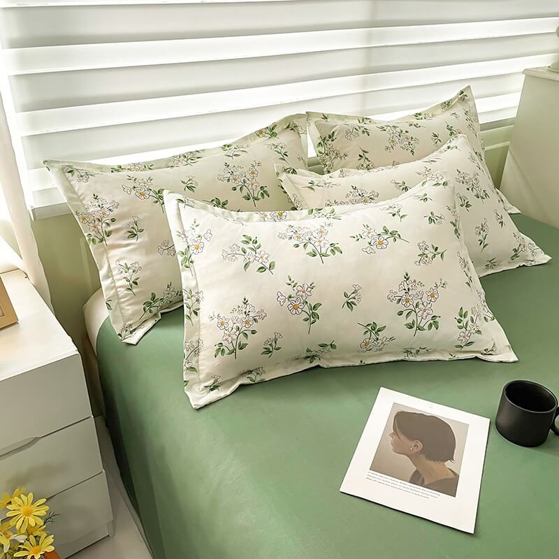 Floral-patterned pillows on a bed with a side table and lamp in a bedroom setting.