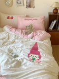 Children's bedroom with pink and white bedding featuring a cartoon character, teddy bear, and checkered pillow.