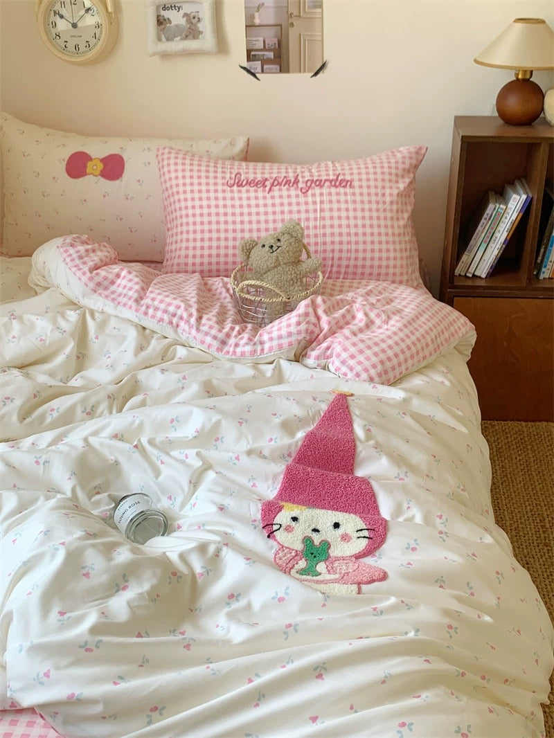 Children's bedroom with pink and white bedding featuring a cartoon character, teddy bear, and checkered pillow.