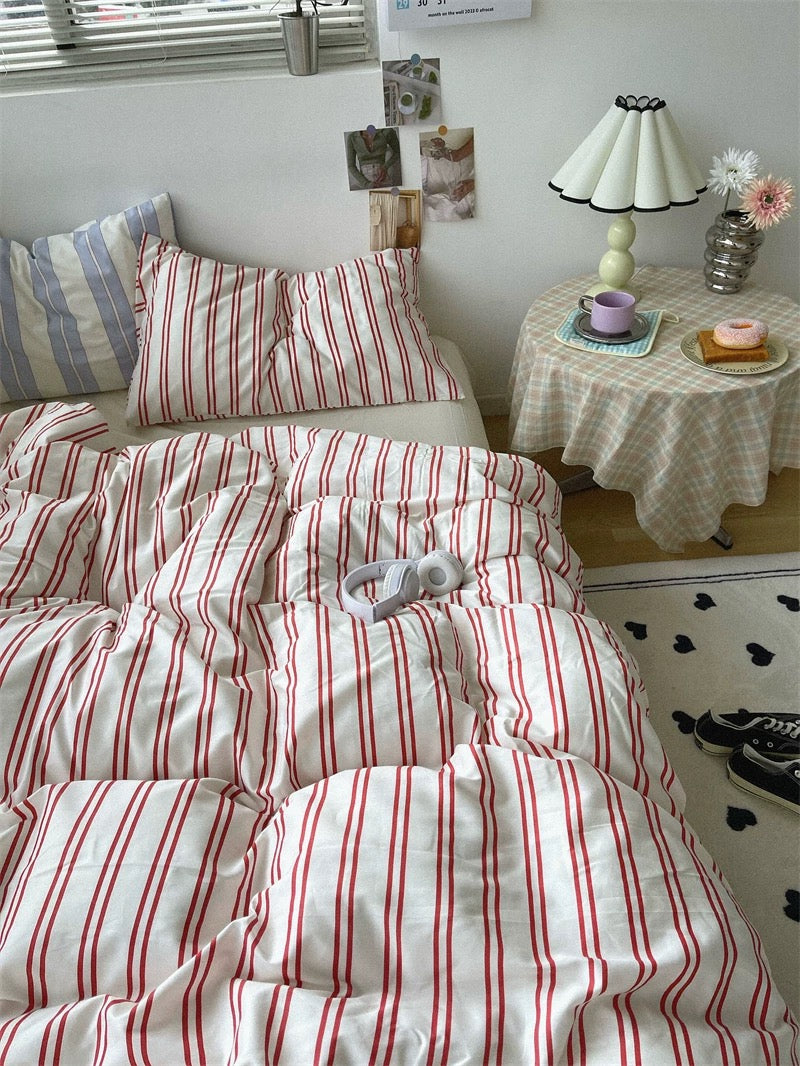Bed with red and white striped bedding in a room with a small table and lamp.