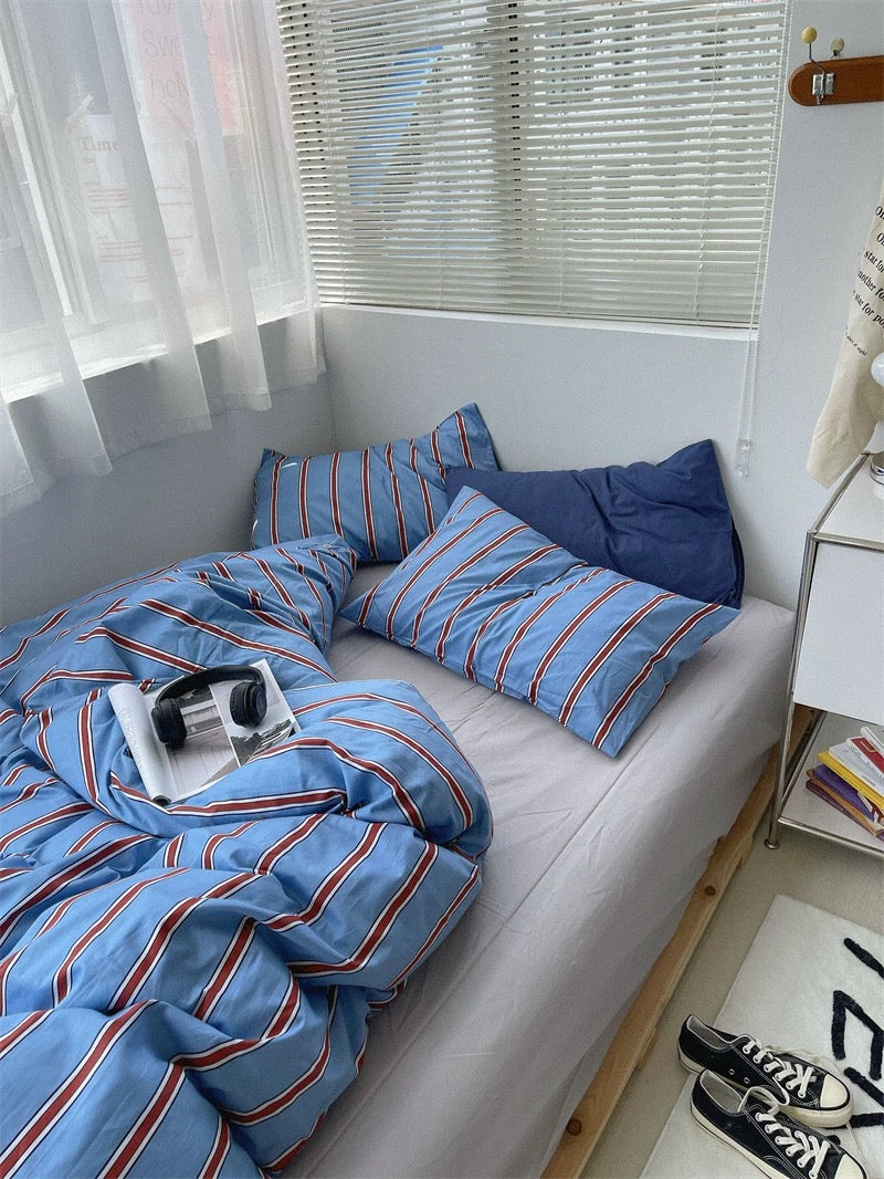 Bed with blue striped bedding and pillows in a bright room.