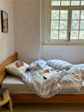 Bedroom with a bed covered in striped bedding and pillows, near a window.
