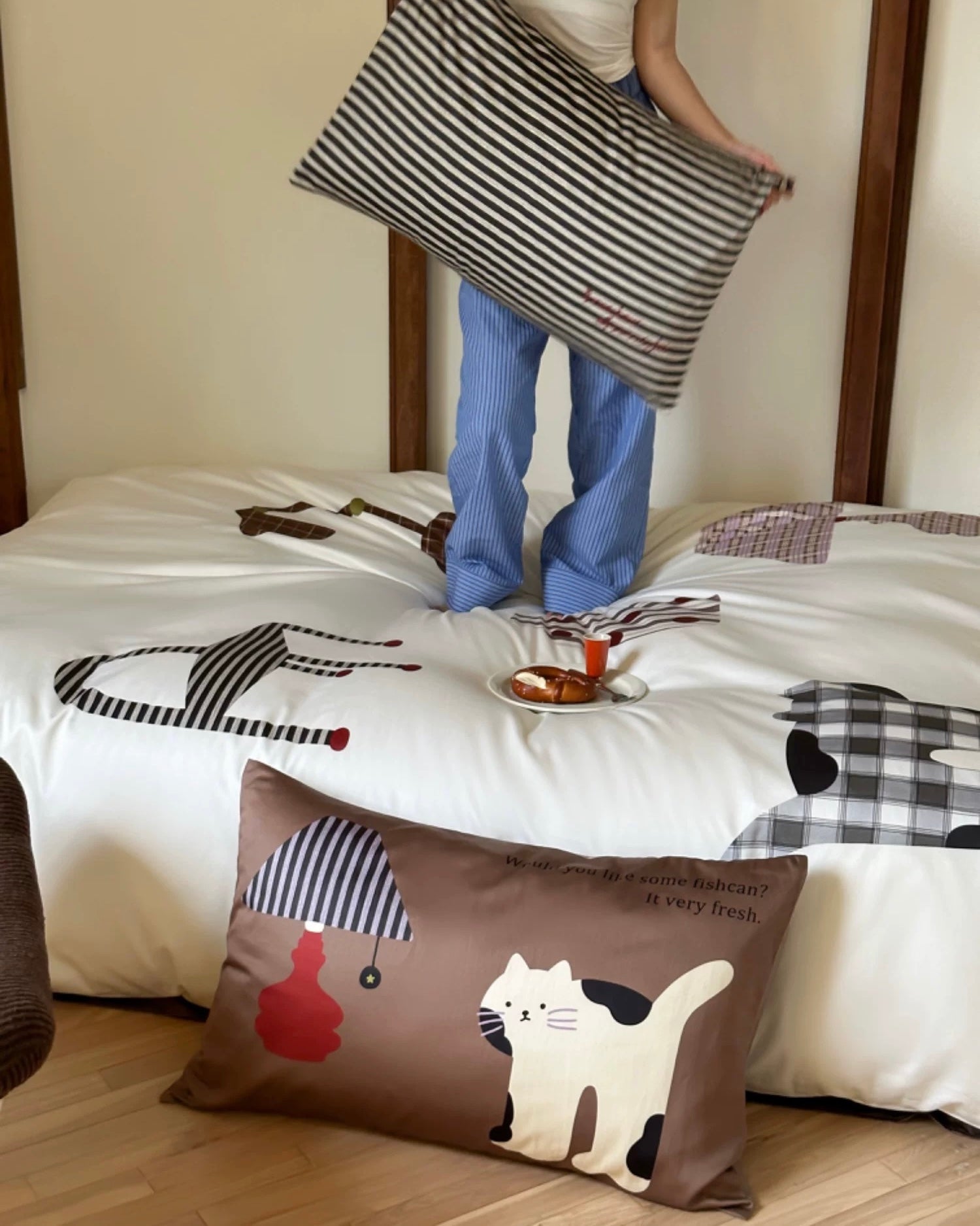 Person holding a striped pillow over a bed with decorative pillows featuring animal designs.