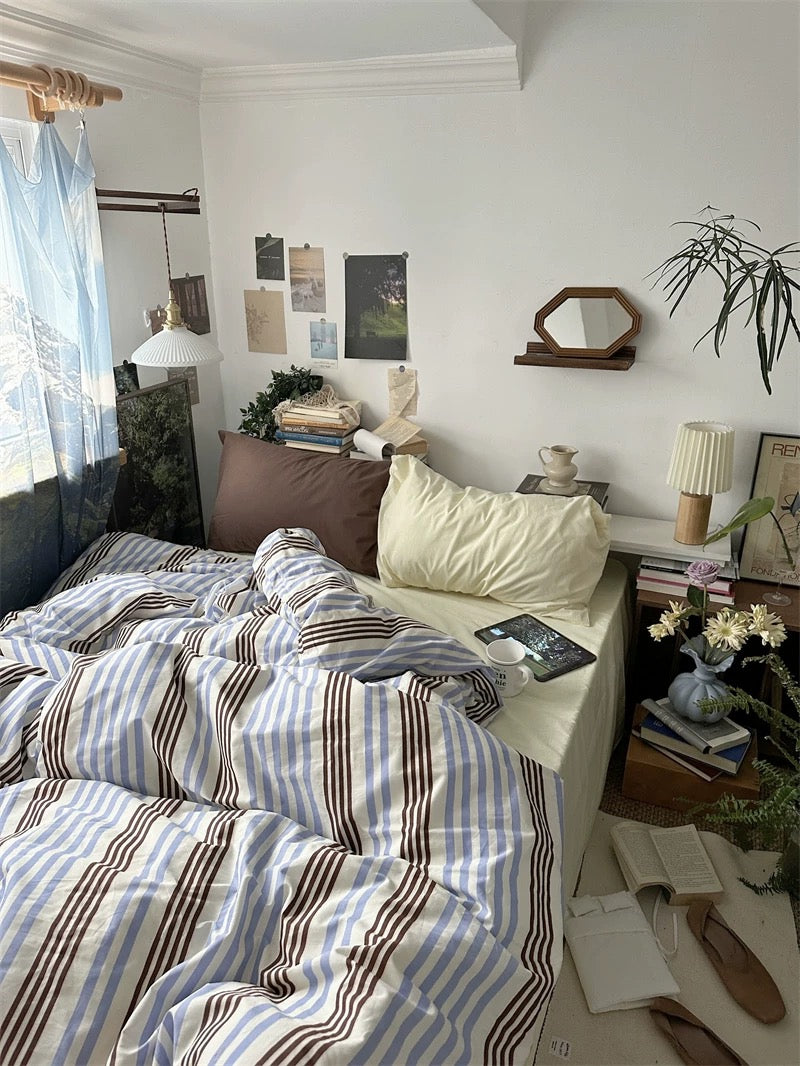 Bedroom with striped bedding, books, and decorative items on a shelf.