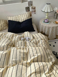 Bed with striped bedding in a room with a small table and lamp.