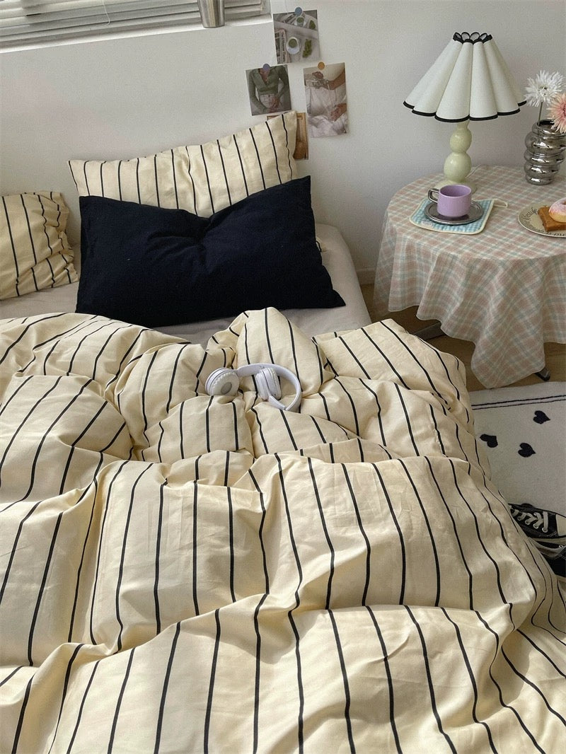 Bed with striped bedding in a room with a small table and lamp.